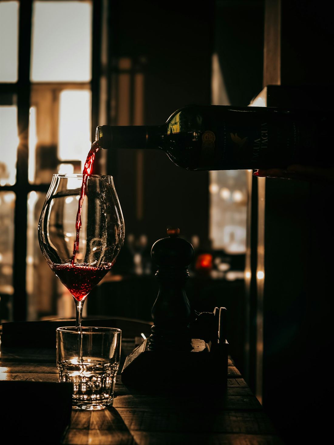 Verre de vin rouge que l'on sert, lumière chaude de fin de journée